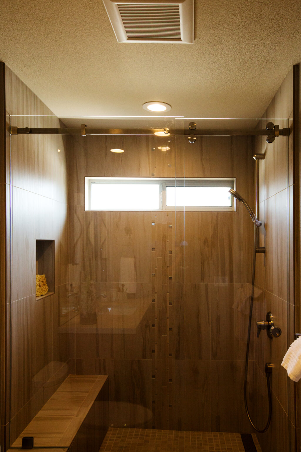 Brushed nickel shower barn door hardware with faux cherry plank wood 15" x 24" porcelain tile walls, transitional interior design.