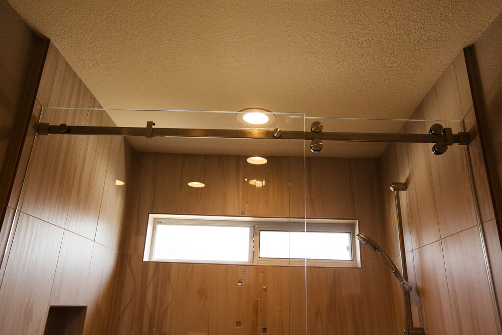 Brushed nickel shower barn door hardware with faux cherry plank wood 15" x 24" porcelain tile walls create contemporary interior design.
